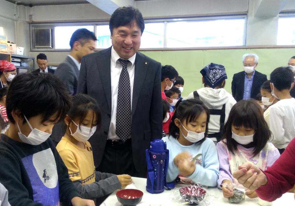 画像：おにぎりを作る児童を見守る斉藤区長2