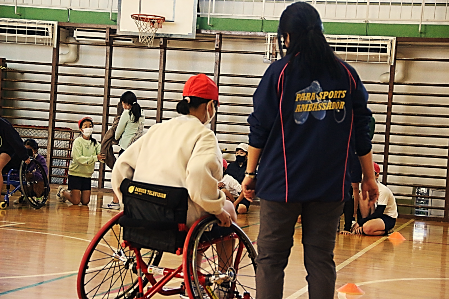 バスケ車に乗る小学生と横について操作説明をするアンバサダー