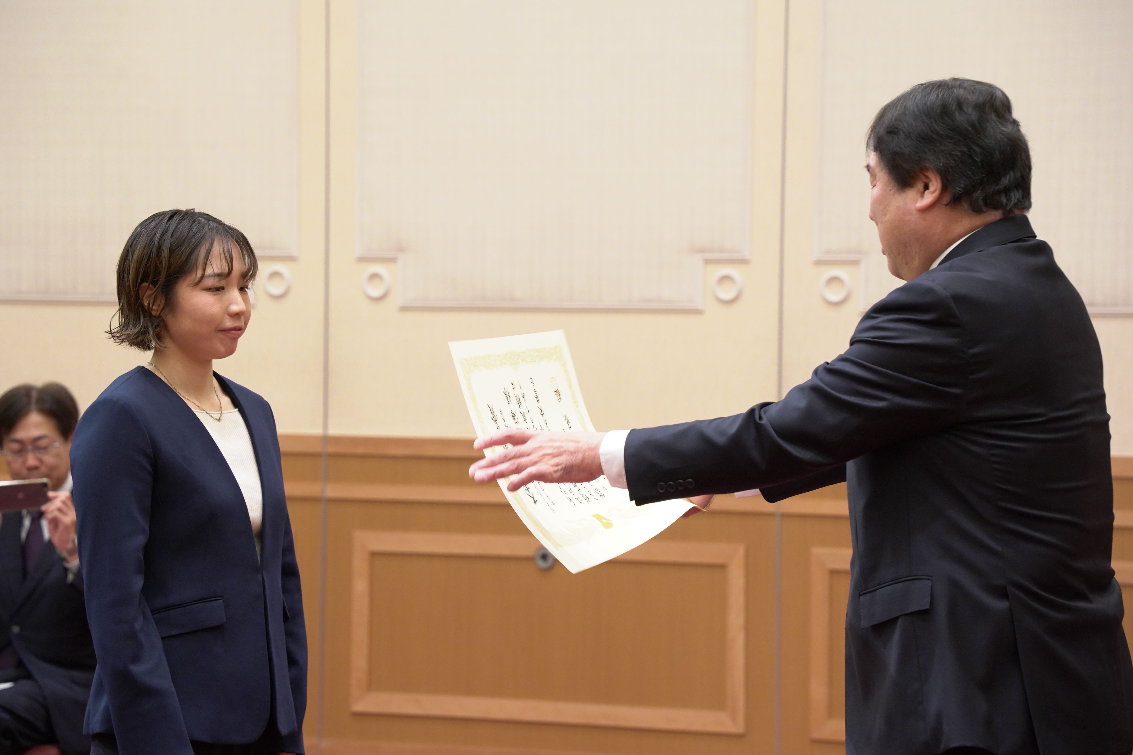 代表挨拶をした岡崎さんへ賞状を授与する斉藤区長