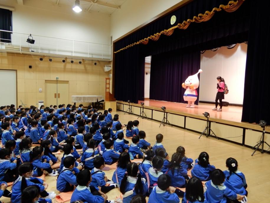 ステージに立つキャラクターとそれを見つめる園児たち