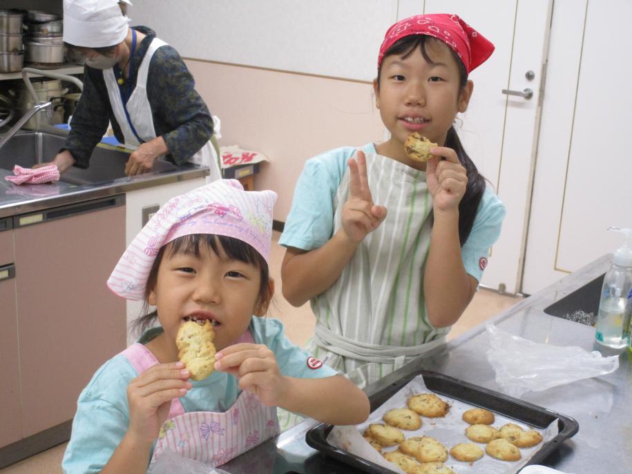 教室の様子。調理台の横に立ち、エプロン姿で美味しそうにクッキーを食べる2人の女の子