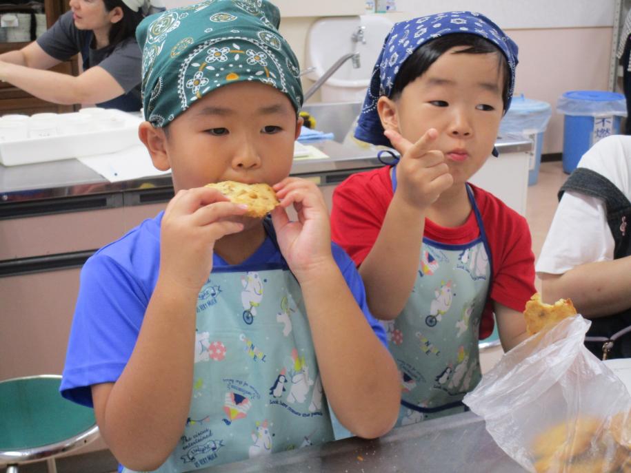 教室の様子。調理台の横に立ち、エプロン姿で美味しそうにクッキーを食べる2人の男の子
