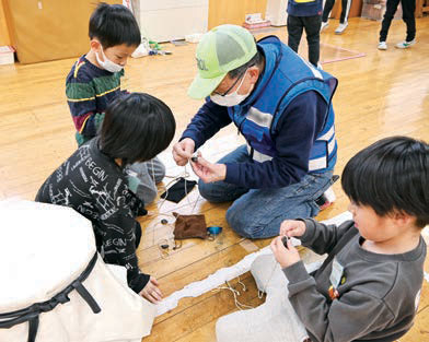 子どもたちにベーゴマをの巻きかたを教える様子