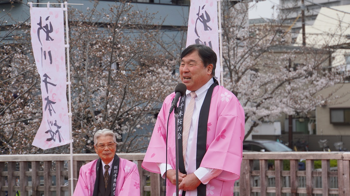 新川千本桜まつりでピンクの法被を着て挨拶する区長