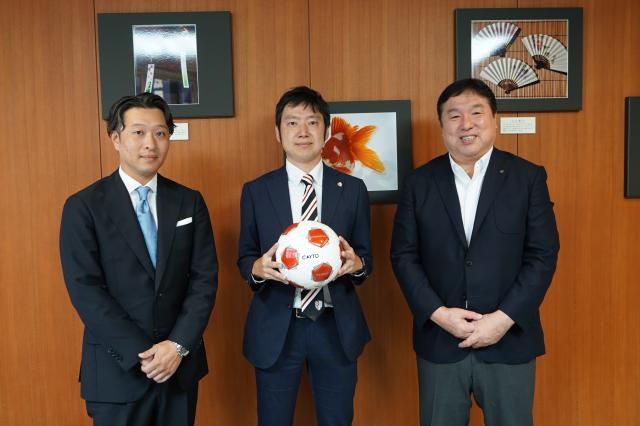 サッカーボールを持つ石井代表取締役社長(中央)、羽島代表取締役(左) 、斉藤区長(右)