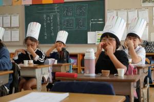 鼻をつまんでグミを食べる児童の様子。紙製のコック帽をかぶっている。